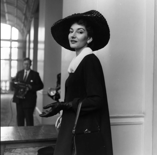 Retrato en blanco y negro de María Callas abrigada caminando por los pasillos de una sala de conciertos.